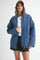 woman wearing a blue quilted jacket over a white top and black denim shorts, styled with a cap