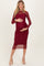 woman wearing a burgundy long sleeve maternity dress with a sheer overlay and holding her baby bump