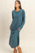 woman wearing a teal long sleeve maxi dress with a pocket and side slits, standing with hands in pockets