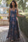 woman wearing a navy floral maxi dress with a deep v-neck and spaghetti straps walking in a garden