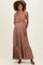 woman wearing a brown pleated maternity maxi dress, gently holding her baby bump