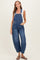 woman wearing a blue denim maternity overall with a fitted bodice and wide legs, styled with a gray tank top