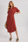 woman wearing a rust-colored button-up midi dress with short sleeves and a collar, accessorized with a straw hat and platform sandals