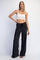 woman wearing a white crop top and black wide-leg pants with pockets, posing with one hand on her hip