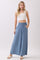 woman wearing a white crop top and blue wide-leg pants with an elastic waistband, standing with one hand in her pocket