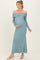 woman wearing a light teal off-shoulder maternity gown with long sleeves and holding her baby bump