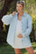 woman wearing a light blue maternity button-up shirt with oversized sleeves and a white tank top, holding her baby bump