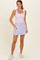 woman wearing a light pink tank bodysuit and a lavender skort with pockets, standing on a neutral background