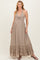 woman wearing a beige halter neck maternity maxi dress with a tie front and tiered ruffle hem, showing her baby bump