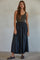 woman wearing a striped sleeveless top and a long black maxi skirt, standing against a neutral background