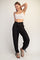 woman wearing a white crop top and black drawstring jogger pants, smiling and posing with one hand on her hip