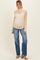 woman wearing a light yellow lace maternity top and blue jeans, showing her baby bump