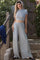 woman wearing a light gray cropped t-shirt and matching wide-leg pants, standing outdoors near a wooden fence