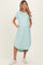 woman wearing a light mint green maternity dress with short sleeves and pockets, showcasing her baby bump