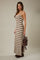 woman wearing a cream and brown patterned spaghetti strap maxi dress with side slits and holding a brown bag