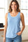 woman wearing a light blue sleeveless top with decorative trim and jeans, standing indoors with a smile