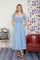 woman wearing a light blue midi dress with puff sleeves and white floral patterns, standing in a room with red and blue decor