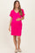 woman wearing a hot pink maternity dress with short sleeves and a v-neck, gently cradling her baby bump