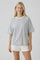 woman wearing a gray oversized t-shirt with a cream trim and white shorts, standing and smiling