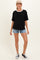 woman wearing a black maternity t-shirt with white trim and denim shorts, styled casually with sneakers and a cap