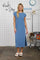 woman wearing a blue cap sleeve maxi dress with a side slit and standing in a laundry-themed setting