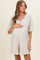 woman wearing a beige short-sleeve maternity dress, holding her baby bump with a v-neckline and pockets