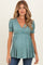 woman wearing a teal maternity top with white floral print and puff sleeves, showing her baby bump