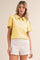 woman wearing a yellow short sleeve polo shirt with button detail and ruffled sleeves, paired with white shorts