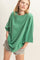 woman wearing an oversized green t-shirt and distressed gray shorts, posing with hands in pockets