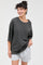 woman wearing an oversized dark gray t-shirt and light gray shorts, smiling and posing casually