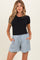 woman wearing a black short sleeve top and light blue maternity shorts with pockets and a tie front.