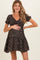 woman wearing a black floral maternity dress with short sleeves, smiling and holding her baby bump
