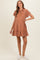 woman wearing a rust-colored short sleeve maternity dress with a button front and ruffle hem