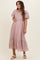 woman wearing a light pink short sleeve maternity dress with embroidered details and a tiered hem