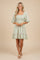 woman wearing a light green short sleeve floral embroidered dress with a smocked bodice and tiered skirt