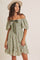 woman wearing a green off-the-shoulder floral dress with puff sleeves and a ribbon tie detail