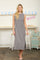 woman wearing a sleeveless gray maxi dress with a side slit, standing in a bright, cheerful setting
