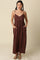 woman wearing a brown maxi dress with thin straps and pockets, standing against a neutral background