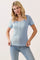 woman wearing a light blue short sleeve top with a button front and scalloped edges, styled with jeans