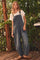 woman wearing a relaxed fit denim overall with a white t-shirt underneath, standing outdoors against greenery