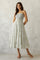 woman wearing a white floral maxi dress with thin straps and a smocked bodice, standing against a neutral backdrop