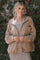 woman wearing a beige corduroy zip-up jacket over a striped dress, smiling against a leafy background