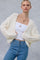 woman wearing a cream cable knit cardigan over a white tank top paired with high-waisted blue jeans