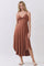woman wearing a rust colored sleeveless midi dress with a knot detail at the front and a high low hem