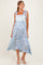 woman wearing a light blue maternity dress with floral patterns and tie straps, styled with a flowy skirt and white sandals