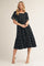 woman wearing a navy blue midi dress with a square neckline and gold floral patterns, styled with short sleeves and a tiered skirt