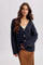 woman wearing a navy textured cardigan with buttons, paired with a cream tank top and a brown polka dot skirt
