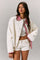 woman wearing a white oversized jacket with a red gingham collar, styled with a white crop top and white shorts