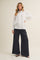 woman wearing a white button-up shirt and black wide-leg pants standing against a neutral background
