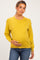 woman wearing a mustard yellow long sleeve maternity sweater and holding her baby bump